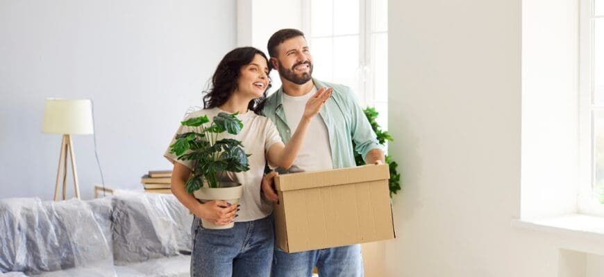 Couple,Moving,With,Boxes,Into,New,Home.,They,Stand,Together